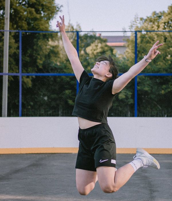 Energetic woman in athletic wear mid-movement against a dark carbon background.
